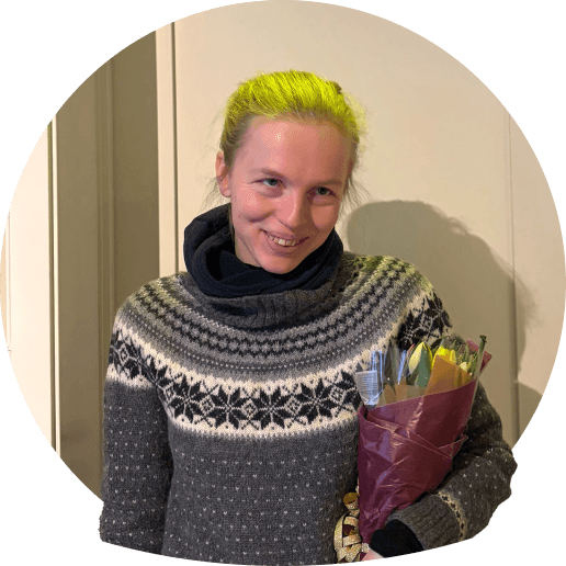 Amalie med lyst hår, iført en grå mønstret trøje, holder en buket blomster.